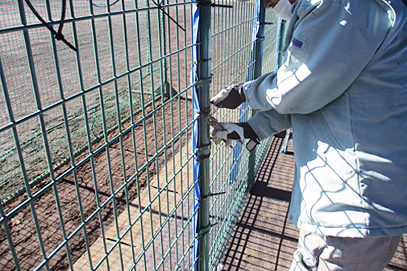 防護マット施工②：ハトメに結束バンドを通してフェンスに取り付けているため、強風でも外れる心配はありません